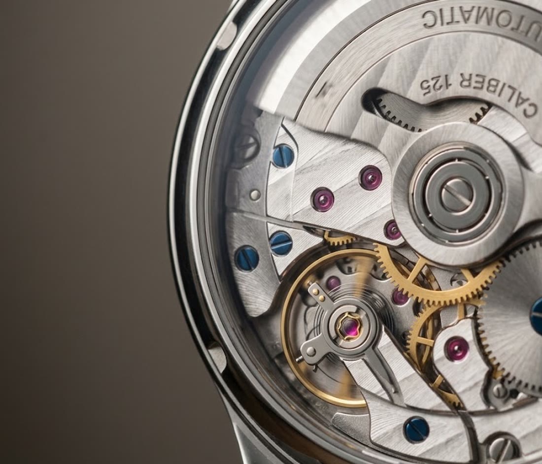 Close-up of a watch movement through the case back: gears, balance wheel and blued screws